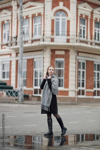 A beautiful young stylish and fashionable girl in a black coat and a gray scarf walks through the city streets