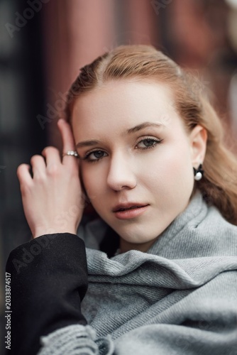 A beautiful young stylish and fashionable girl in a black coat and a gray scarf walks through the city streets