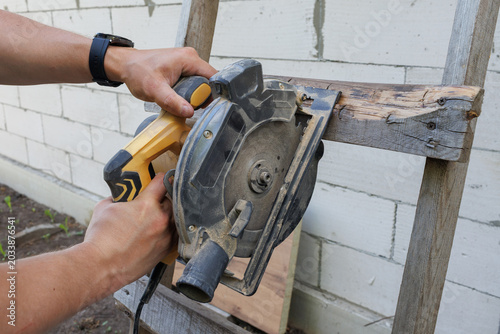 Fotografi A person cuts a horizontal wooden rung of a ladder using a circular power saw ne