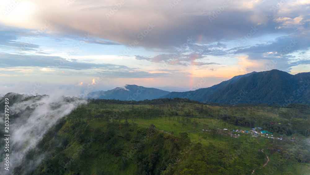 Fototapeta premium An aerial view of a pine forested mountaintop, with fog and a rainbow in the morning.