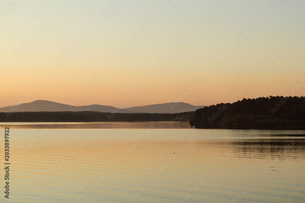 Fototapeta premium Summer sunset nature landscape, panoramic view of mountain and water surface at sunset, summer solstice background, peaceful scene of a lake in golden hour