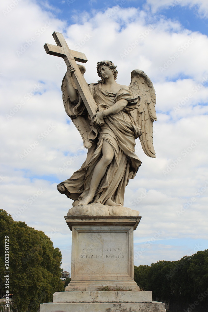 Obraz premium A majestic marble angel statue holding a cross, silhouetted against a bright, cloudy sky in Rome.