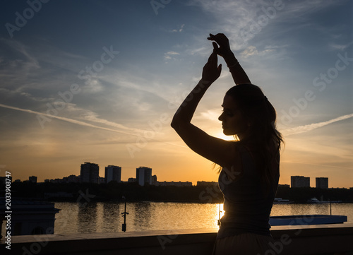 Fényképezés silhouette of a girl against the backdrop of a sunset on the river on a summer d