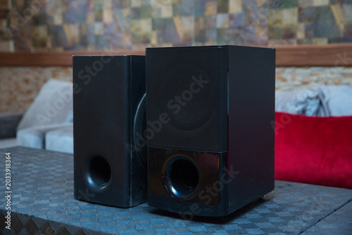 interior, providing high quality loud audio sound and home theater entertainment . Modern black LG stereo speakers with a subwoofer subsystem are placed on a textured dark table in a cozy living room