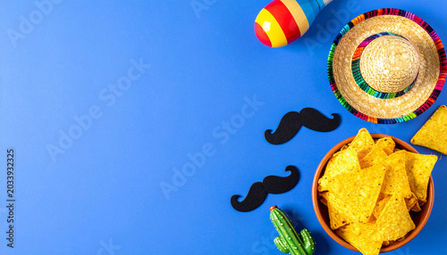 Fiesta Essentials: A vibrant arrangement of festive elements, including a sombrero, maracas, nachos, and a miniature cactus, are scattered across a bright blue surface, evoking a lively celebration.