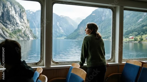 Woman looking at a scenic fjord view through a ferry window, reflective travel moment, serene tourism concept, dramatic landscape, calm atmosphere, soft natural light, realistic window and water