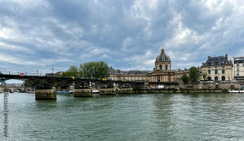 Pont des Arts bridge across the Seine River in Paris under dramatic cloudy skies with the Institute of France in the background.