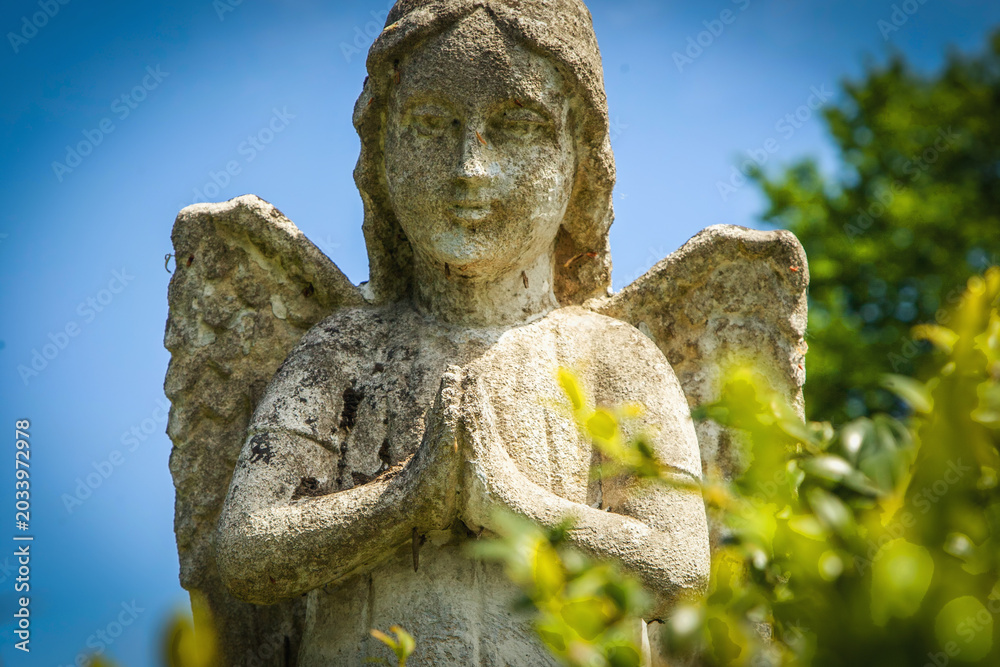Obraz premium Guardian angel statue praying under blue summer sky.