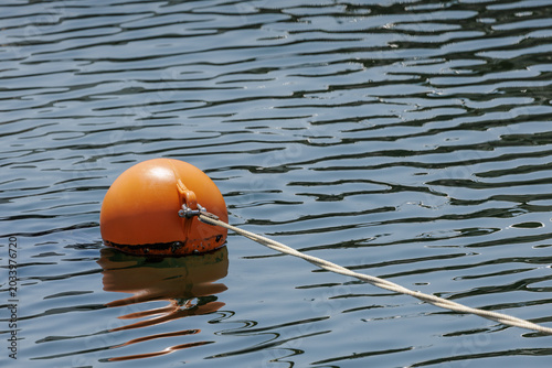 Foto Orange mooring buoy tethered with white rope stretching into the distance in calm rippled water