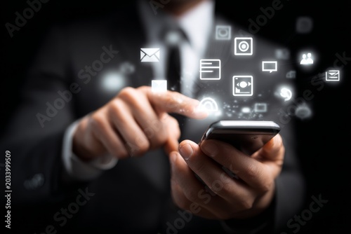 Professional Businessman Using Smartphone with Digital Communication Icons on Black Background for Modern Technology and Connectivity Concepts