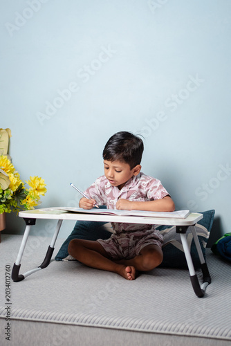 Young Indian boy studying at a portable desk on the floor, focused on his schoolwork