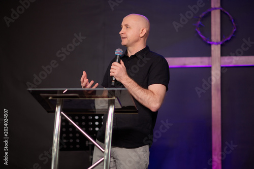 Emotional Christian preacher speaking with microphone and gesture church during worship gathering