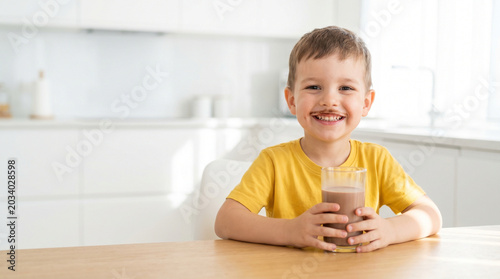 Smiling boy holding a glass of chocolate milk at home kitchen  