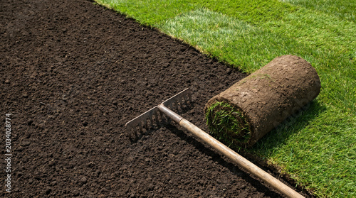 Freshly prepared soil with rolled sod and garden rake in sunlight  