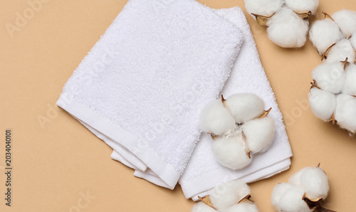 Valokuva A folded soft white terry towel and natural cotton bolls on a warm beige background symbolize purity and comfort