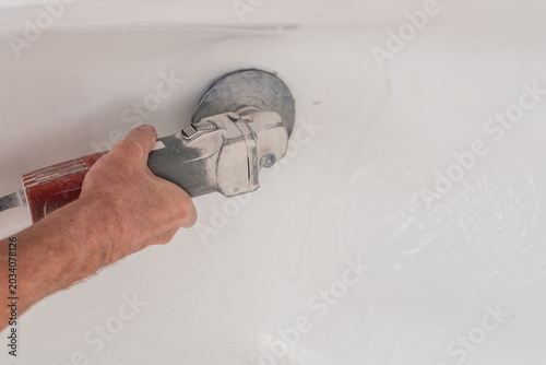 Closeup photo of man polishing bath tub surface with special tool. Worker polishing bathtub bottom with power grinder tool