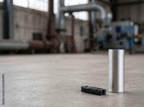 Stainless thermos and folded multitool on concrete floor in an industrial warehouse environment for product showcase and background