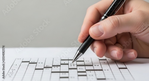Hand solving crossword puzzle with black pen on white background. Crossword grid filled with letters in neat arrangement, providing an enjoyable challenge for puzzle enthusiasts.
