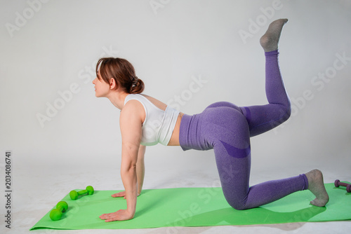 Kneeling leg lift butt toning Donkey Kick exercise, young sportive woman exercising in the studio on a fitness mat, isolated on white background, strength training buttocks with pilates exercises 