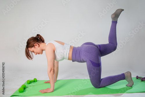 Kneeling leg lift butt toning Donkey Kick exercise, young sportive woman exercising in the studio on a fitness mat, isolated on white background, strength training buttocks with pilates exercises 