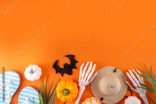Summerween holiday background. Bright festive background for summer Halloween holiday in style of Halloween with summer decorations, pumpkins, ghost, bat, summer vacation accessories, tropical leaves