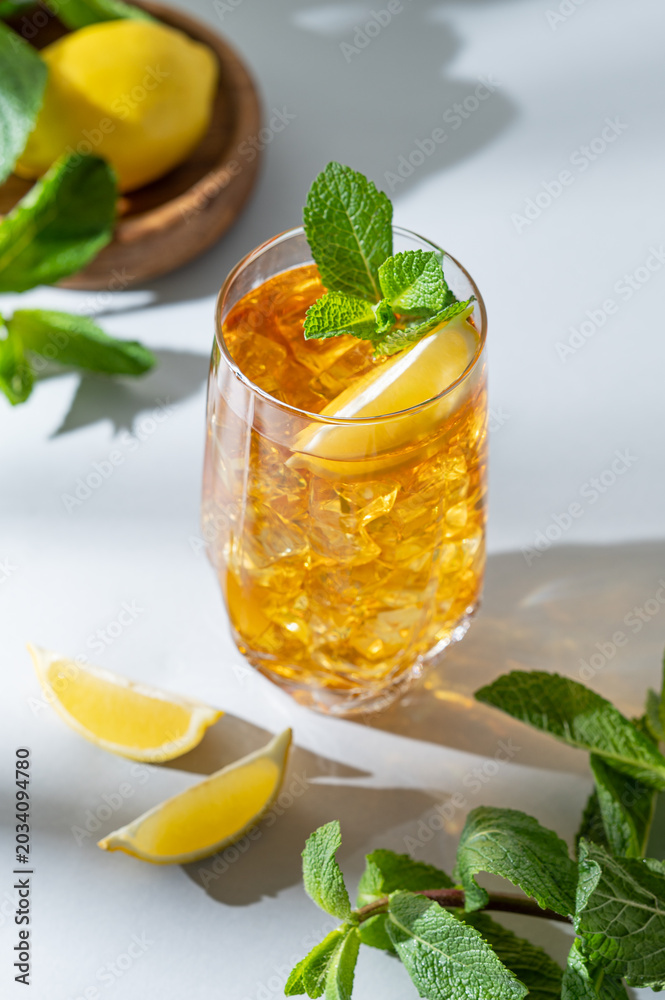 Fototapeta premium Iced tea with lemon and mint in a glass on a light background with shadows