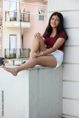 Asian girl in maroon crop top and white skirt seated on windowsill barefoot carefree mood