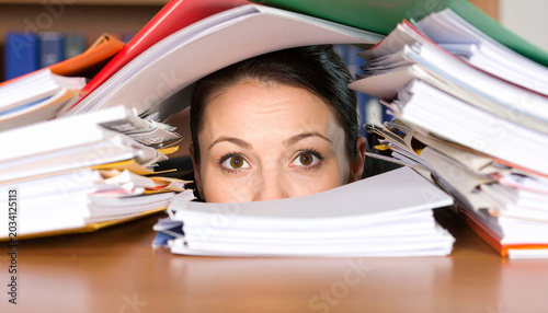 Wide eyed person buried under piles of documents. Documents overflow desk area. Individual appears stressed by workload and paperwork chaos