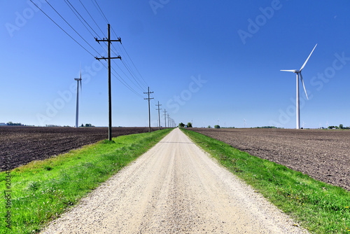 Принти на полотні An unpaved road splices between telephone poles and a wind turrbine while stretching to and vanishing at the horizon