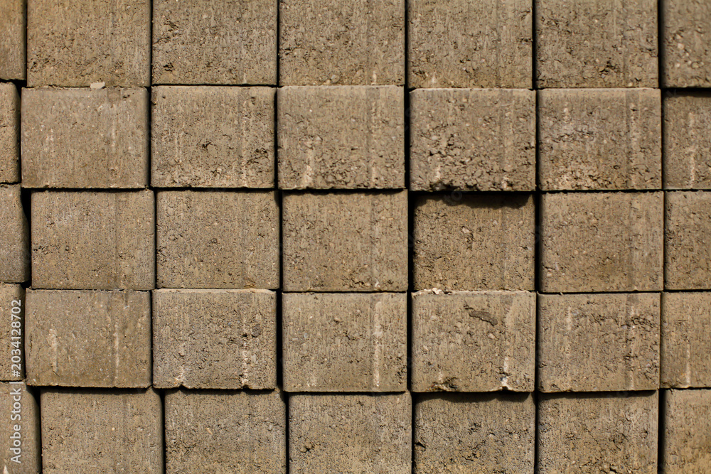 Fototapeta premium Close-up of stacked concrete paving blocks with rough industrial texture and geometric pattern. Construction material background for architecture and infrastructure themes