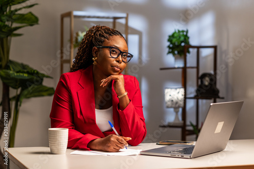 Bild auf Leinwand African corporate businesswoman thinking, writing notes in her office