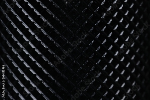 Macro shot of black textured metal surface with diamond knurling pattern. Close up of non-slip ribbed grip texture with selective focus, perfect for industrial, tech, and sports concepts.