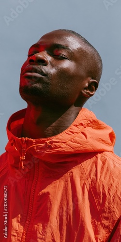 Close-up moody portrait of a man in an orange hooded jacket with red side lighting for fashion background and editorial banner
