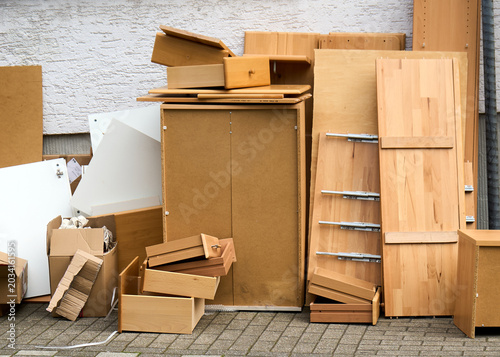 Konstfotografi Ein Haufen von ausrangierten Holzmöbeln, Schränken, Schubladen und Kartons steht als Sperrmüll auf dem gepflasterten Gehweg vor einer weißen Hauswand