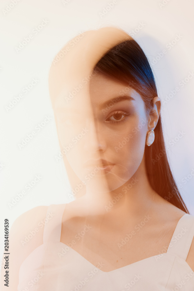 Fototapeta premium Portrait of a young woman with long hair wearing white earrings and a white top. Soft lighting creates a dreamy fashion and beauty concept with artistic blur effects.