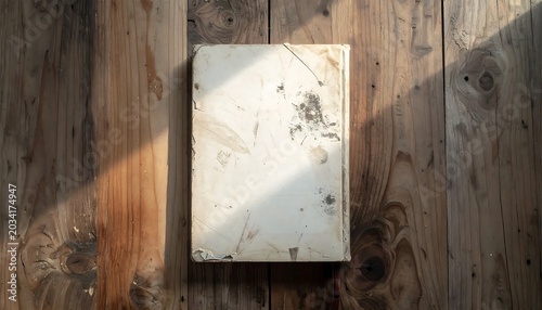 Worn White Book Resting on Rustic Wooden Table in Soft Sunlight