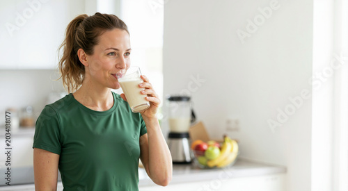 Smiling woman drinking a protein meal replacement shake in a modern kitchen. Healthy lifestyle and weight loss diet concept