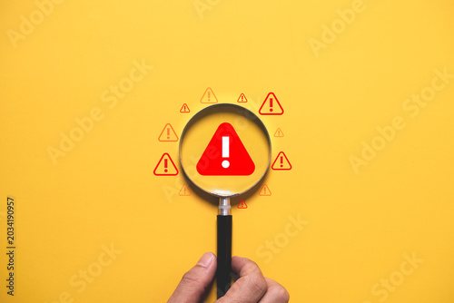 Photos Warning alert concept with magnifying glass focusing on danger symbol over yellow background
