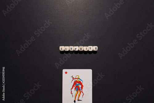 Obraz na płótnie Surprise spelled with letter tiles above a joker card on dark background, symbolizing unexpected events, wildcard advantage and risk