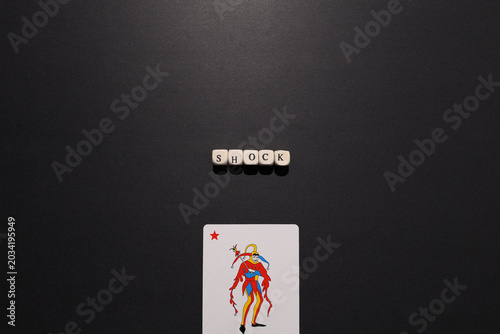 Foto Shock spelled with letter tiles above a joker card on dark background, representing sudden events, crisis, surprise and disruption