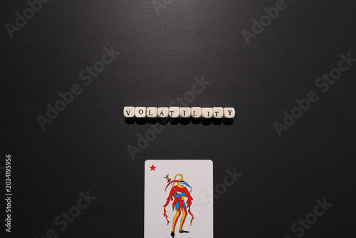 Bild auf Leinwand Volatility spelled with letter tiles above a joker card on dark background, symbolizing market swings, uncertainty and financial risk