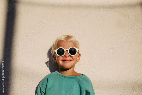 Smiling blond child wearing round sunglasses in warm sunlight.