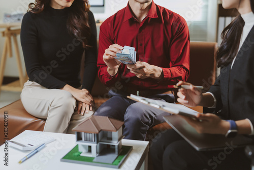 Couple meeting with a real estate agent, negotiating a home purchase. Man paying a down payment or mortgage, sealing the property deal