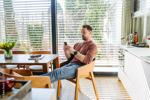 Man sitting in chair and browsing phone at home.