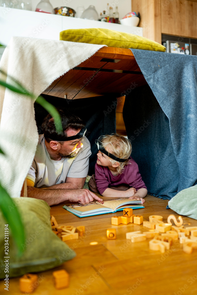 Obraz premium Dad and child building and reading book in cozy blanket fort.