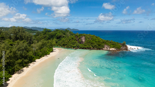 Clear turquoise waters with gentle waves hitting a serene white sandy beach, surrounded by greenery. Seychelles, Mahe. Grand Anse.