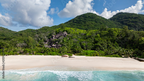 White sandy beach with turquoise water and lush green hills in the background. Seychelles, La Digue. Grand Anse.