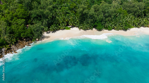 Clear turquoise waves break gently on the white sand beach, backed by dense greenery. Anse Soleil. Seychelles, Mahe.