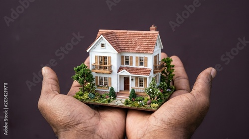 Cupped hands holding miniature house model with landscaping real estate concept