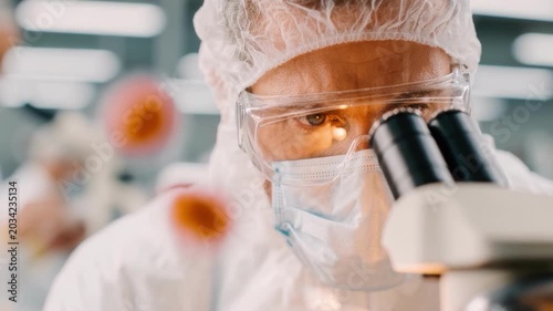 Cleanroom technician inspects vial under microscope, wearing protective suit, hairnet, goggles and mask, amber lighting and sterile background, careful handling of sample in controlled pharmaceutical